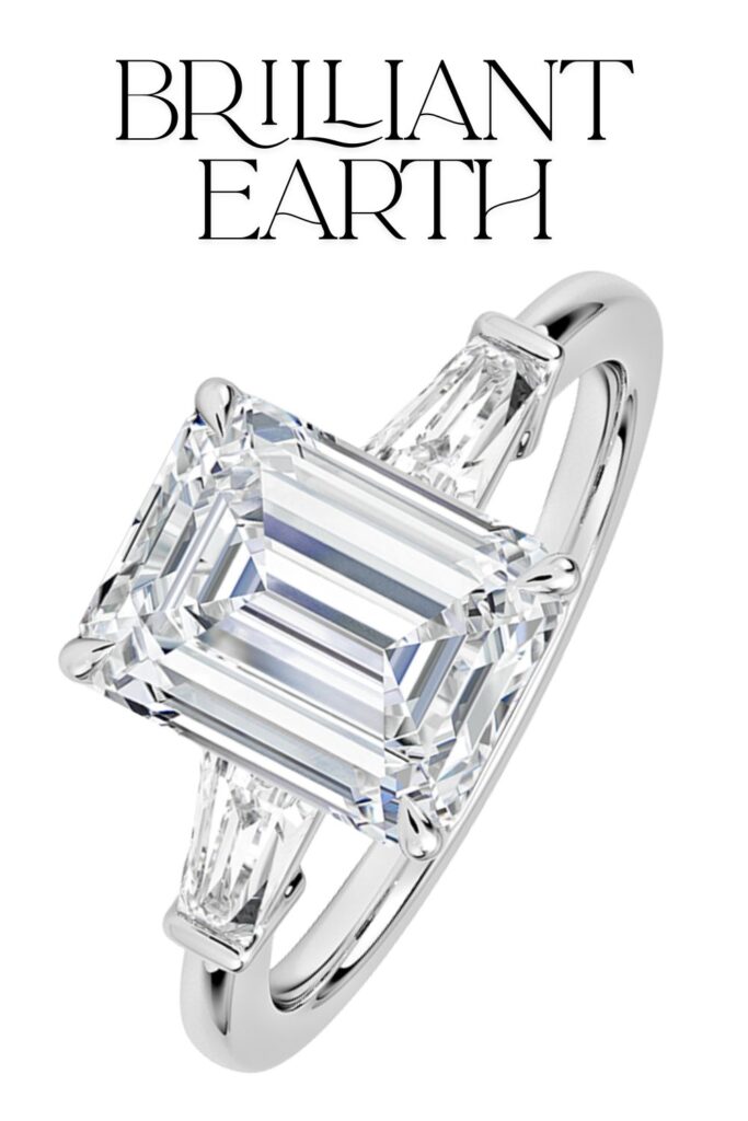 The Brilliant Earth Symphony Tapered Baguette Three Stone Diamond Ring features a striking emerald-cut center diamond of impeccable clarity and color, flanked by tapered baguette diamonds, all set in lustrous 18K white gold. The three-stone design showcases exquisite craftsmanship, accentuating the brilliance of each diamond while maintaining an elegant and timeless aesthetic. The polished band enhances the overall design, making it a captivating choice for an engagement ring.