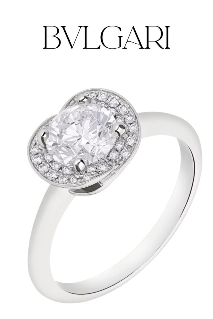The Bvlgari Incontro d’Amore Ring features a stunning round brilliant-cut diamond at its center, surrounded by a halo of pavé diamonds, all set in luxurious platinum. The elegant band is sleek and minimalist, enhancing the ring's overall brilliance and sophistication. This design showcases exceptional craftsmanship, combining modernity with classic charm.