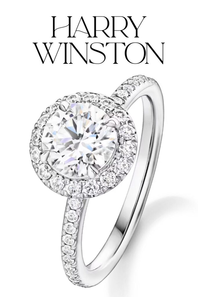 This Harry Winston engagement ring features a stunning round brilliant diamond at its center, enhanced by a halo of smaller diamonds, creating a radiant effect. The setting is a micropavé style, where the band is adorned with additional diamonds, crafted in high-quality platinum for a luxurious finish. The overall design exemplifies elegance, highlighting the exceptional cut, clarity, and color of the main diamond.