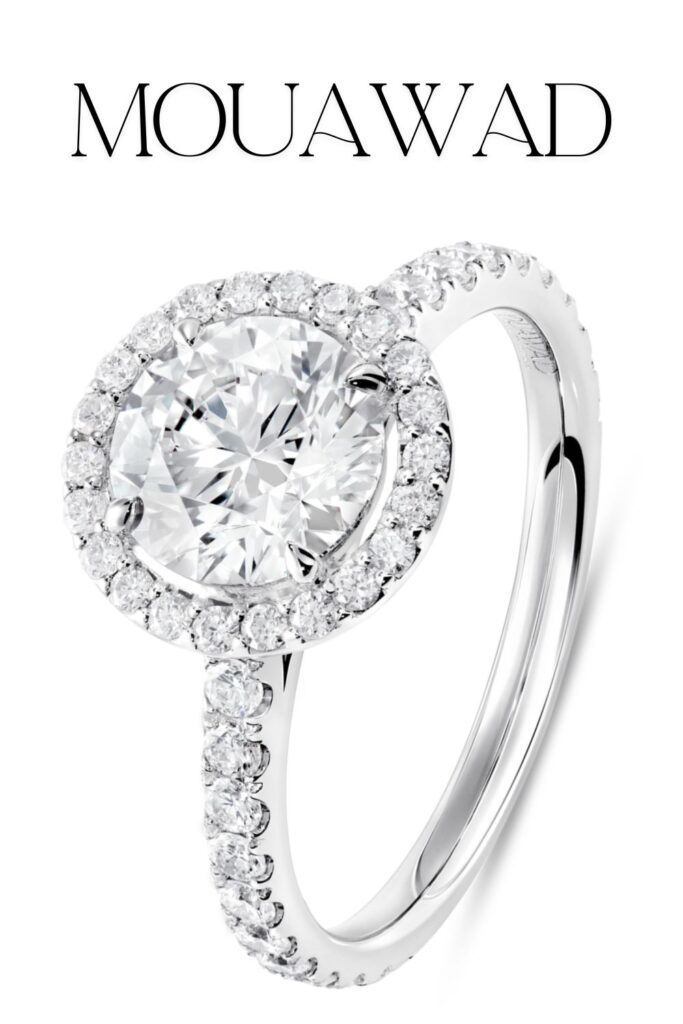 The Mouawad Unity engagement ring features a stunning round brilliant diamond at its center, surrounded by a sparkling micropavé halo and a band adorned with additional pavé stones, all meticulously set in gleaming white gold. The elegant design highlights the diamond's exceptional clarity and brilliance, making it a captivating choice for an engagement ring.