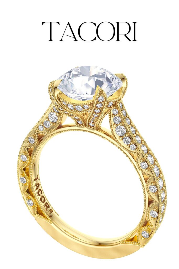 The Tacori Classic Crescent engagement ring features a stunning round solitaire diamond set in 18kt yellow gold, showcasing exceptional clarity and brilliance. The intricately designed band, adorned with pavé-set diamonds along its sides, highlights the craftsmanship and elegance characteristic of the Tacori brand. The delicate detailing complements the timeless design, making it a captivating choice for any engagement.