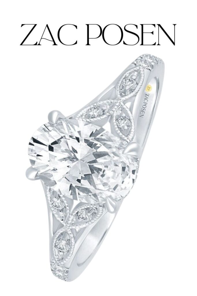 An elegant Zac Posen engagement ring features a stunning oval-cut lab-grown diamond, approximately 1 3/4 carats, set in a beautifully designed 14K white gold band. The band showcases intricate, swirling details adorned with smaller round diamonds, enhancing the ring's overall brilliance and sophistication. The combination of the central diamond's clarity and color, paired with the delicate metalwork, exemplifies exquisite craftsmanship.