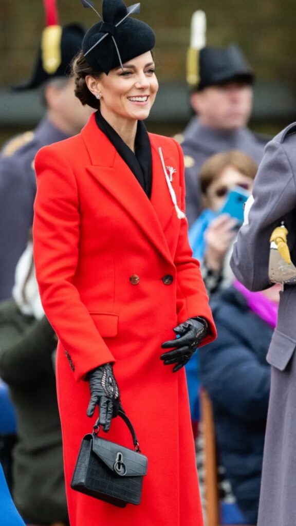 The black croc Amberley handbag from Mulberry adds an element of sophistication to Kate Middleton's striking red coat ensemble. The bag features a structured silhouette with a top handle, complementing the tailored shape of her double-breasted coat, while its textured finish contrasts beautifully with the smooth fabric and enhances her overall look. Paired with elegant gloves and a black scarf, it underscores a polished and cohesive aesthetic.