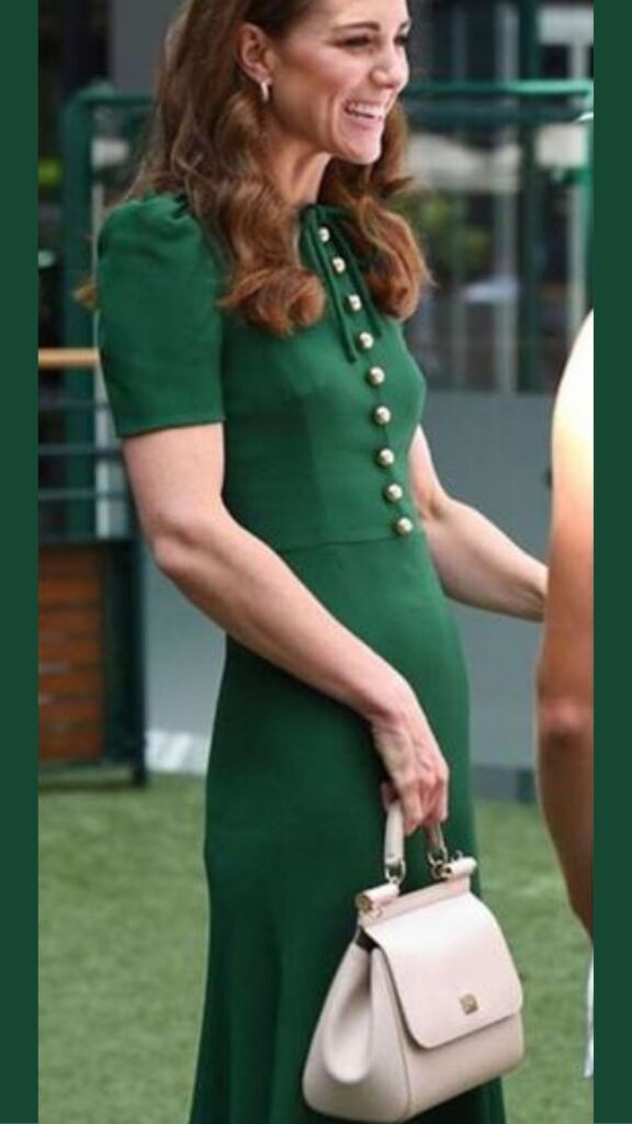 The Dolce & Gabbana Sicily Bag in rose complements Kate Middleton's elegant green dress, featuring a fitted silhouette with a high neckline and button detailing, accentuating her sophisticated style. The soft pink hue of the handbag creates a striking contrast against the rich green, while its structured shape adds a refined touch to her overall look. This combination highlights her fashion sense, balancing classic elegance with modern chic.