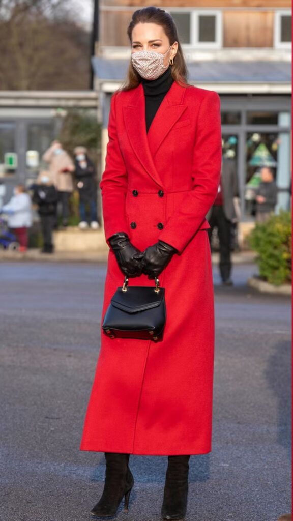 The handbag worn by Kate Middleton is the Grace Han Small Love Letter Bag in black, which complements her bold red double-breasted coat, adding a touch of elegance and sophistication. The structured silhouette of the bag, with its distinctive flap closure and gold-tone accents, provides a refined contrast to the tailored look, while the small size maintains a chic balance against the coat's length. This thoughtful accessory choice enhances her polished appearance, seamlessly uniting style and functionality.
