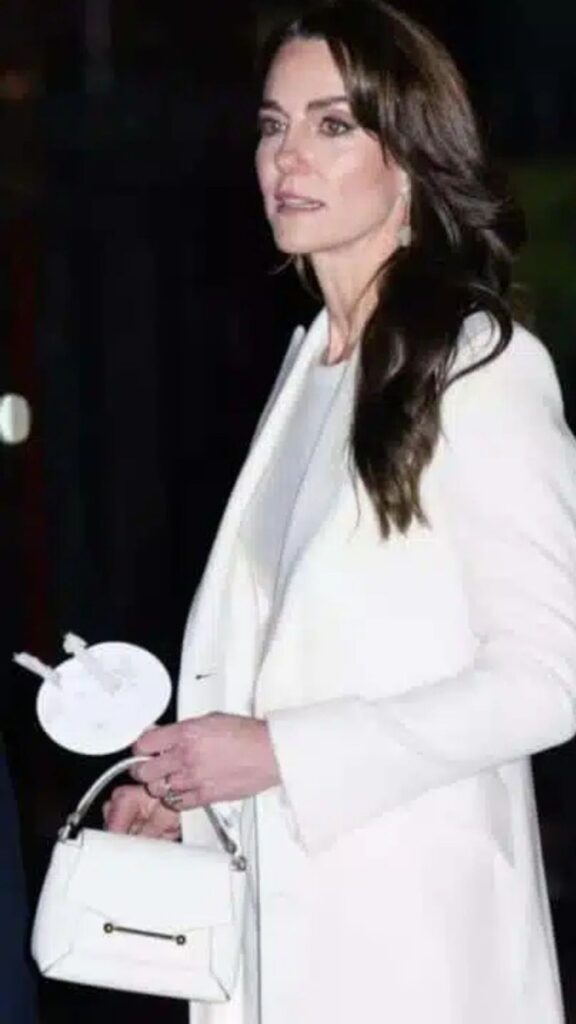 The Strathberry ‘Mosaic’ Nano Bag in Vanilla complements Kate Middleton's sophisticated look, featuring a sleek, structured design that pairs elegantly with her tailored white coat. The handbag's minimalist aesthetic, accentuated by a subtle gold clasp, enhances the overall monochromatic palette, which includes a simple white top beneath her blazer. This polished accessory adds a modern touch to her classic style while maintaining a refined elegance.