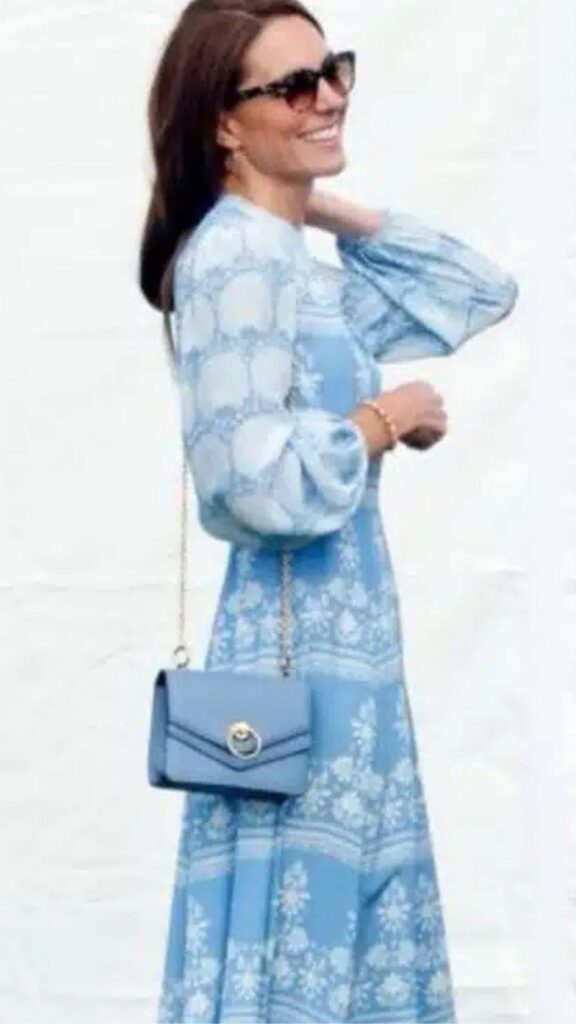 Kate Middleton accessorizes her light blue printed dress with a Mulberry Harlow Satchel in Cloud Blue, complementing the garment's soft hues and floral motifs. The bag’s structured silhouette and slim chain strap add an elegant touch while maintaining a balanced, polished look. Its chic design enhances the overall outfit, highlighting refined sophistication and a cohesive color palette.