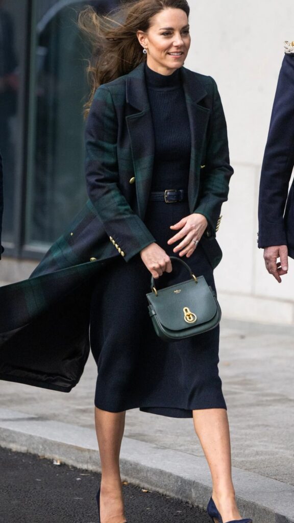 Kate Middleton showcases the Mulberry Small Amberley Satchel in a rich green, complementing her tailored, dark ensemble consisting of a fitted turtleneck and a long plaid coat. The structured silhouette of the handbag adds a polished touch to her chic, sophisticated look, enhancing the outfit's elegant color palette while blending function and fashion seamlessly.