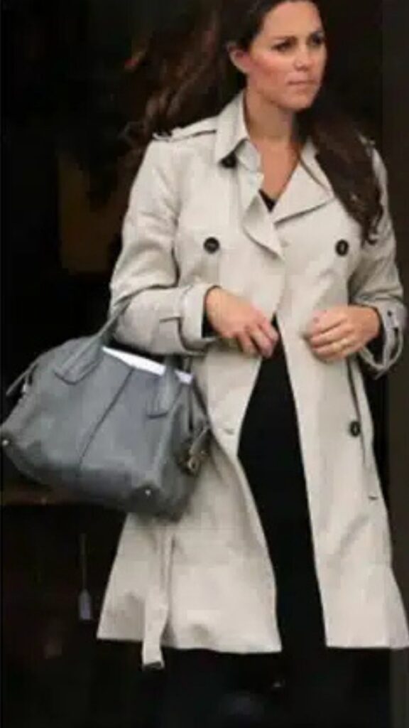 Kate Middleton carries a Tod's D-Styling Bauletto Bag in dove grey, seamlessly complementing her light beige trench coat and sleek black ensemble. The structured silhouette of the handbag enhances her polished look, while the neutral color adds a sophisticated touch that balances the outfit's layered elements. Features like the bag's dual handles and subtle hardware lend practicality and elegance to her overall appearance.