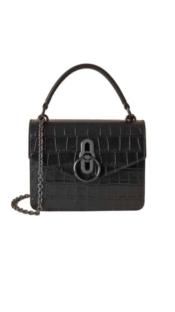 The black croc-embossed Amberley handbag by Mulberry features a structured silhouette with a top handle and a detachable chain strap for versatile wear. It is adorned with a distinctive black metal clasp, enhancing its modern elegance. The glossy finish of the croc pattern adds a sophisticated touch to this chic accessory.