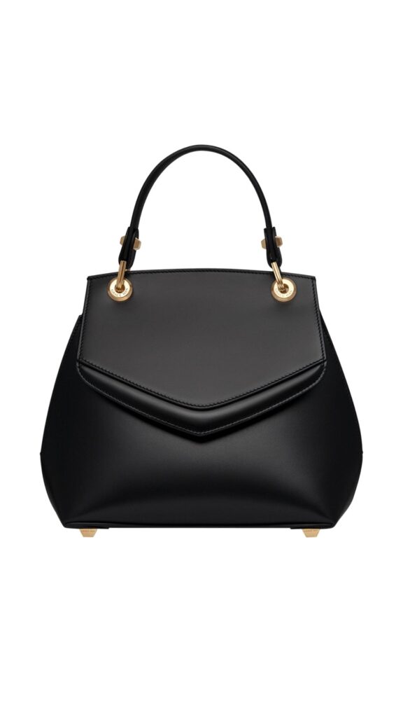 The Grace Han Small Love Letter Bag features a structured silhouette with a unique angular flap and a rounded body, crafted in sleek black leather. It is accented with gold-tone hardware and a top handle that adds elegance and versatility for carrying. The bag's minimalist design highlights its sophisticated texture and timeless appeal.