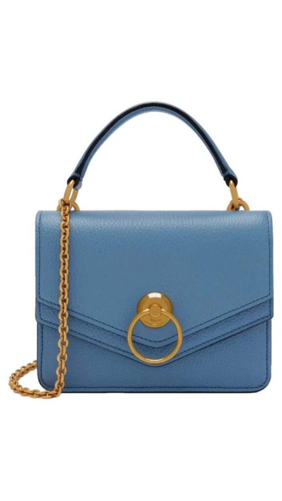 The Mulberry Harlow Satchel features a structured silhouette with a front flap and a distinctive gold circular hardware detail at the center. In a soft cloud blue color, it includes both a top handle and a detachable gold chain shoulder strap for versatile carrying options. Made from textured leather, this handbag combines elegance with functionality.
