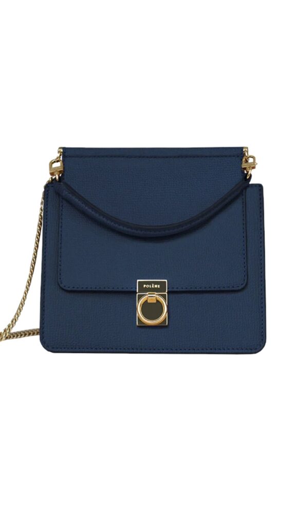 The Polène Paris Number Seven Mini Bag features a structured rectangular silhouette with a fold-over flap secured by a gold-toned circular clasp and an adjustable chain strap. It is crafted from rich blue grain leather, offering a refined yet versatile aesthetic suitable for various occasions. The design balances elegance and practicality, making it an ideal accessory for both casual and formal ensembles.