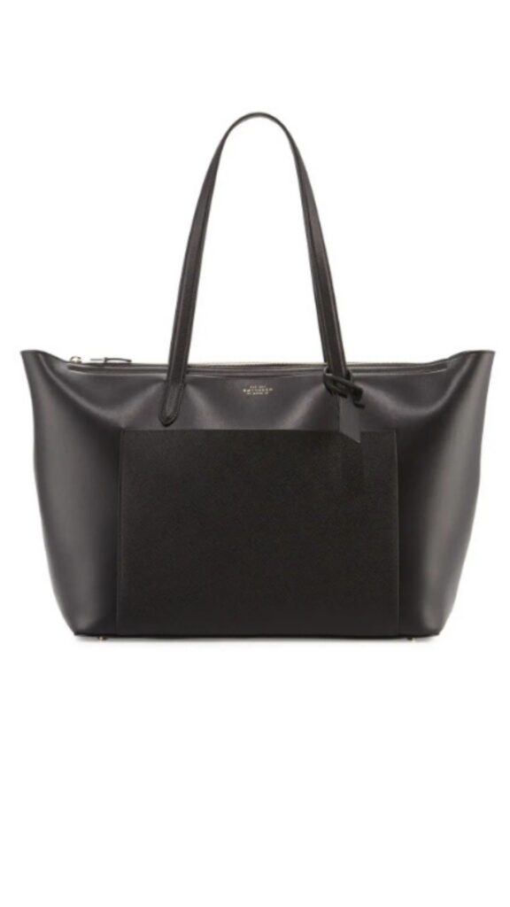 The Smythson Panama East West Zip Tote features a spacious, structured silhouette with a sleek design. It is crafted from high-quality leather in a solid black color, highlighting both elegance and versatility, and includes two sturdy handles for easy carrying. The bag is complemented by a zip closure that enhances security while adding a polished touch.