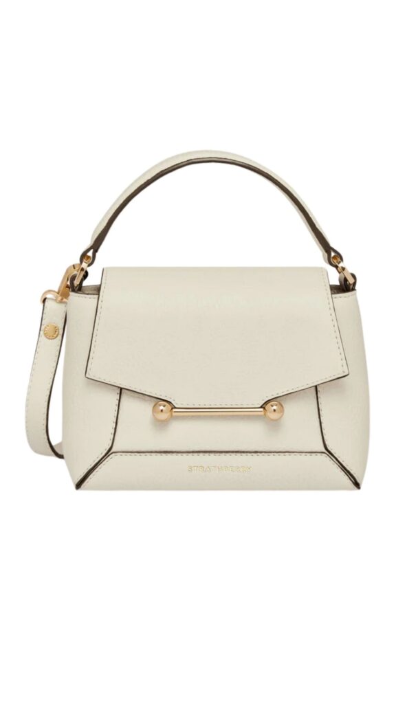 The Strathberry ‘Mosaic’ Nano Bag features a structured silhouette with a top handle and a detachable shoulder strap for versatile carrying options. Crafted in a soft vanilla hue, it is accented with gold-tone hardware including a signature bar closure and the brand name embossed on the front. This compact purse offers a chic, minimalist aesthetic suitable for both casual and formal occasions.