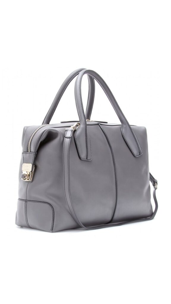 The Tod's D-Styling Bauletto Bag in Dove Grey features a sleek, structured silhouette with dual top handles for easy carrying, complemented by a detachable shoulder strap for versatility. Its smooth, dove grey leather exudes sophistication, while subtle gold-tone hardware adds a touch of elegance. Clean stitching lines along the edges further enhance its timeless design.