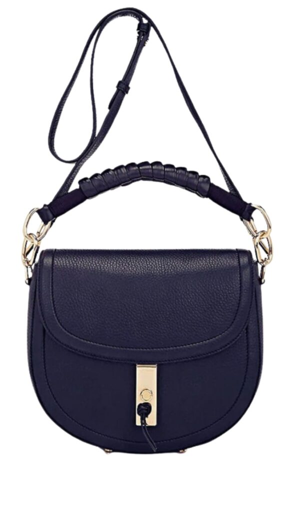 The Altuzarra Ghianda Saddle Bag features a curved silhouette with a structured flap design and a sleek gold clasp at the center. It is crafted from rich navy leather and has a top handle with braided detailing, complemented by a removable shoulder strap for versatile wear. The elegant shape and sophisticated color make it a refined accessory suitable for various occasions.