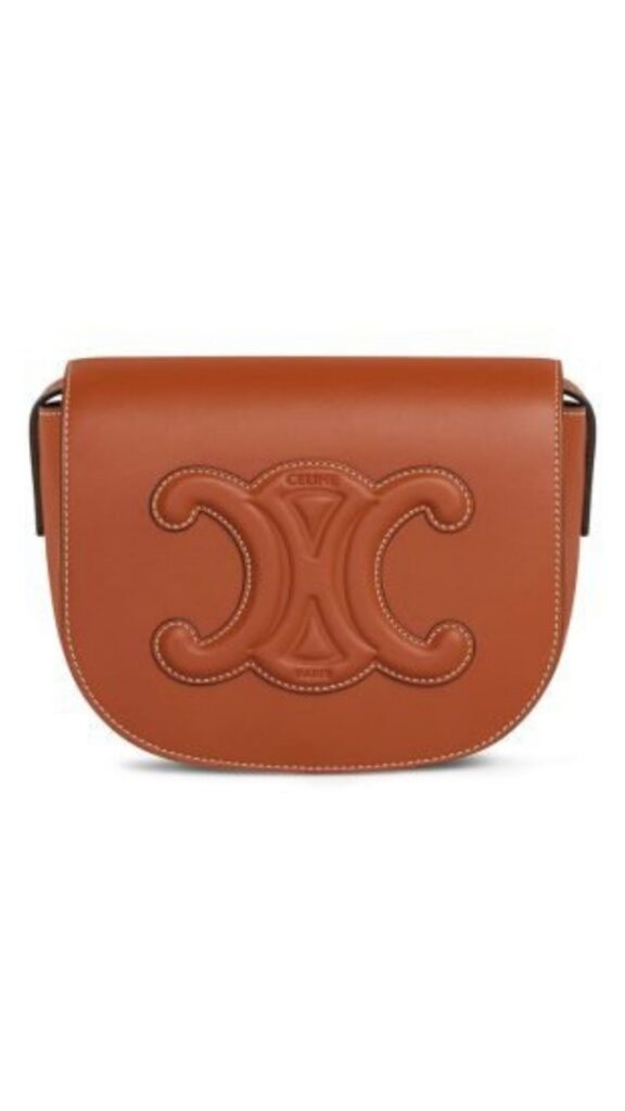 The Celine Folco Cuir Triomphe Shoulder Bag features a sleek, rounded silhouette crafted from tan smooth calfskin leather, with a prominent embossed “C” logo on the front. It is accented with contrasting white stitching, adding an elegant touch, and is designed with a single shoulder strap for versatile wear. This sophisticated piece combines style and functionality, making it a staple accessory.