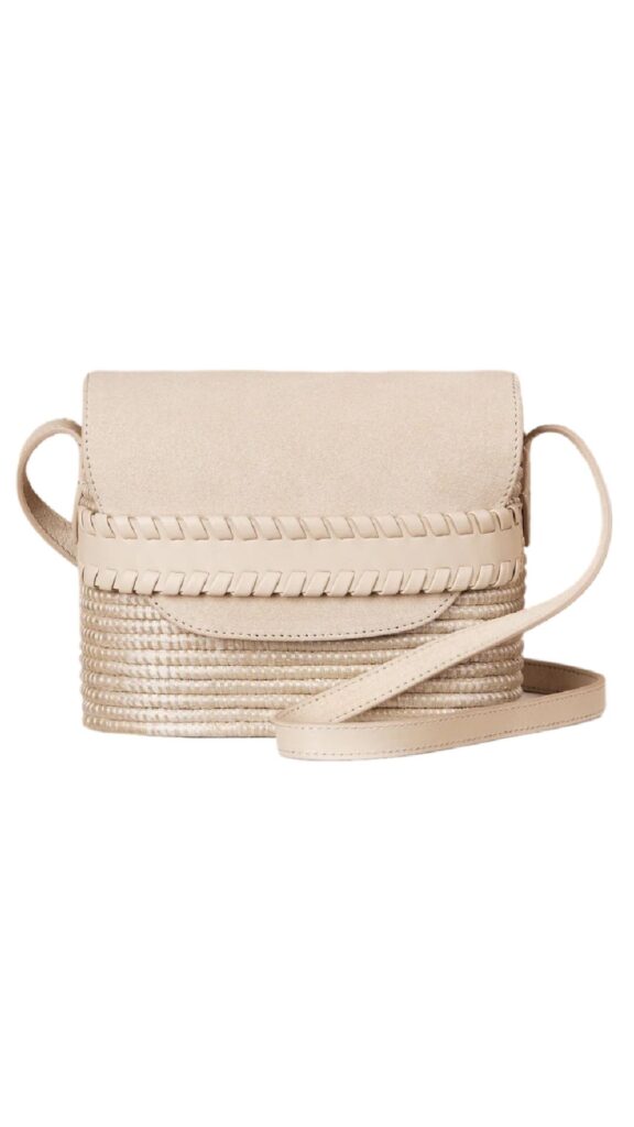 The Cesta Collective Crossbody in Panna Suede features a sleek rectangular silhouette with a braided leather accent along the edges. Its soft beige color is complemented by a luxurious suede finish, and the adjustable strap allows for versatile wear. The bag's subtle texture and minimalistic design make it an elegant accessory for various occasions.