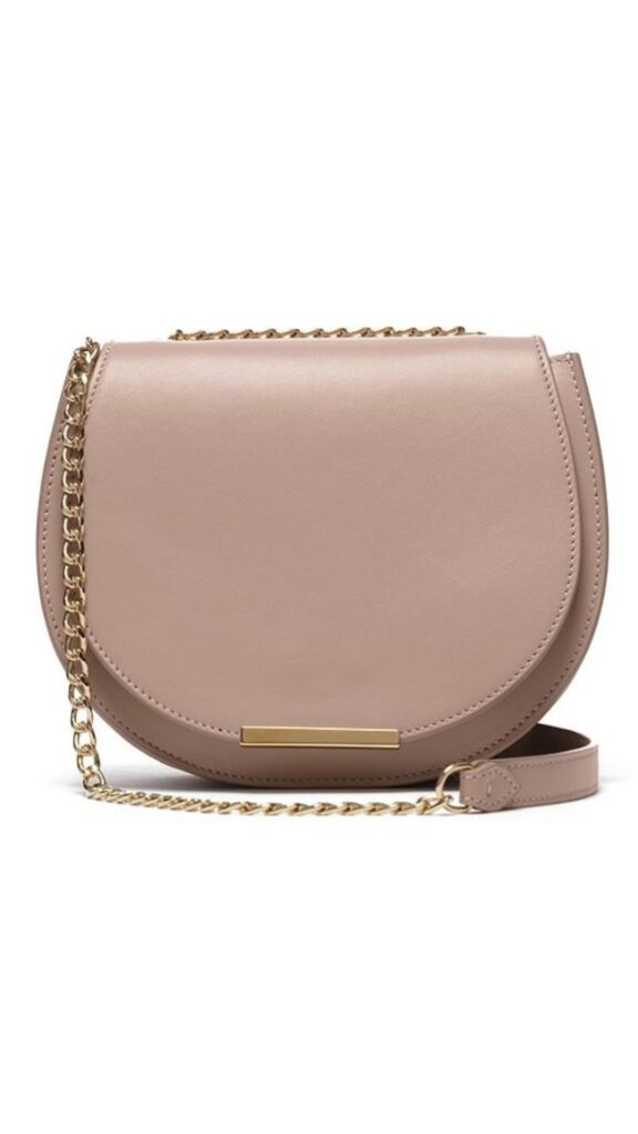 The Cuyana Mini Chain Saddle Bag features a classic half-moon silhouette with a smooth leather exterior in a soft Quartz Dusty Pink hue. It includes a gold-tone chain strap and a minimalistic gold bar detail on the front, blending elegance with modern functionality. This compact handbag is designed for easy access and versatile styling, suitable for both casual and formal occasions.