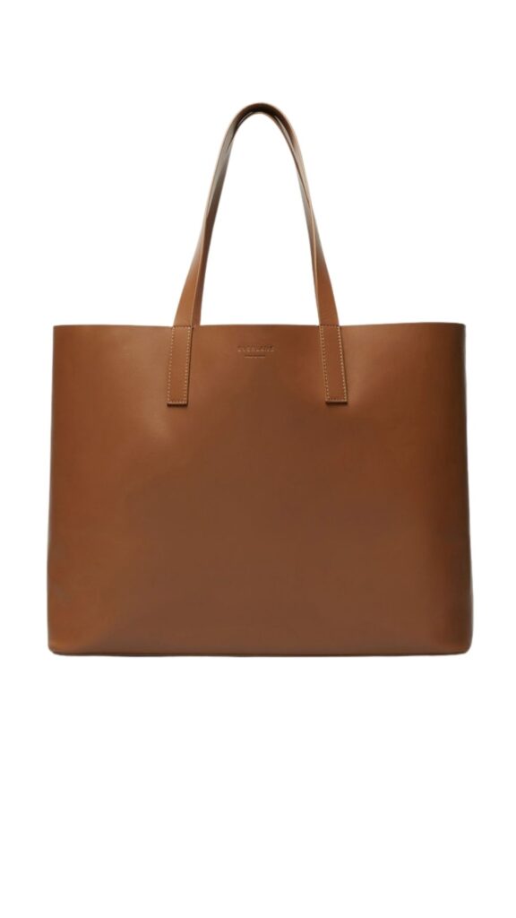 The Everlane Day Market Tote is a sleek, minimalist handbag featuring a structured silhouette with two sturdy top handles. It is made from rich cognac leather, showcasing a smooth finish with subtle stitching details. The bag's design emphasizes functionality with ample interior space, ideal for everyday use.
