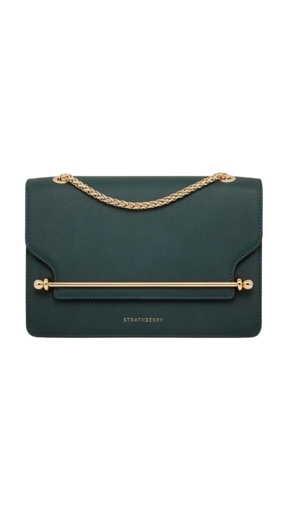 The Strathberry East/West Mini handbag in bottle green features a sleek, rectangular silhouette with a flap closure and a gold-tone chain strap. Its smooth leather exterior is accented by a signature gold bar detailing at the front, adding a touch of elegance. This compact purse melds modern style with functionality, perfect for both casual and formal occasions.
