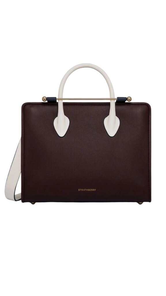 The Strathberry Midi Tote features a structured silhouette with a sleek design, showcasing a rich burgundy leather exterior paired with white accents. It includes elegant top handles and a detachable shoulder strap, complemented by a gold-tone bar closure. The front displays the Strathberry logo, enhancing its sophisticated appeal.