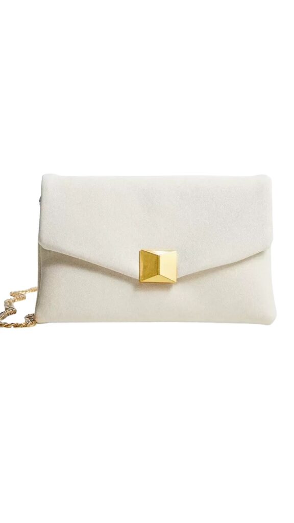 The Valentino Garavani One Stud Shoulder Bag features a sleek, envelope-style silhouette with a smooth ivory exterior. It is adorned with a bold, geometric gold stud closure at the front and includes a delicate chain strap for versatile wear. The minimalist design and soft color make it an elegant choice for any occasion.