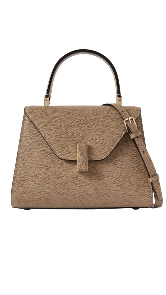 A refined Valextra Iside Mini Tote featuring a structured silhouette with a clean, angular design. The bag is crafted from textured beige leather, accented by a glossy black handle and a matching detachable strap for versatile styling options. A sleek, minimalist flap closure completes its sophisticated look.