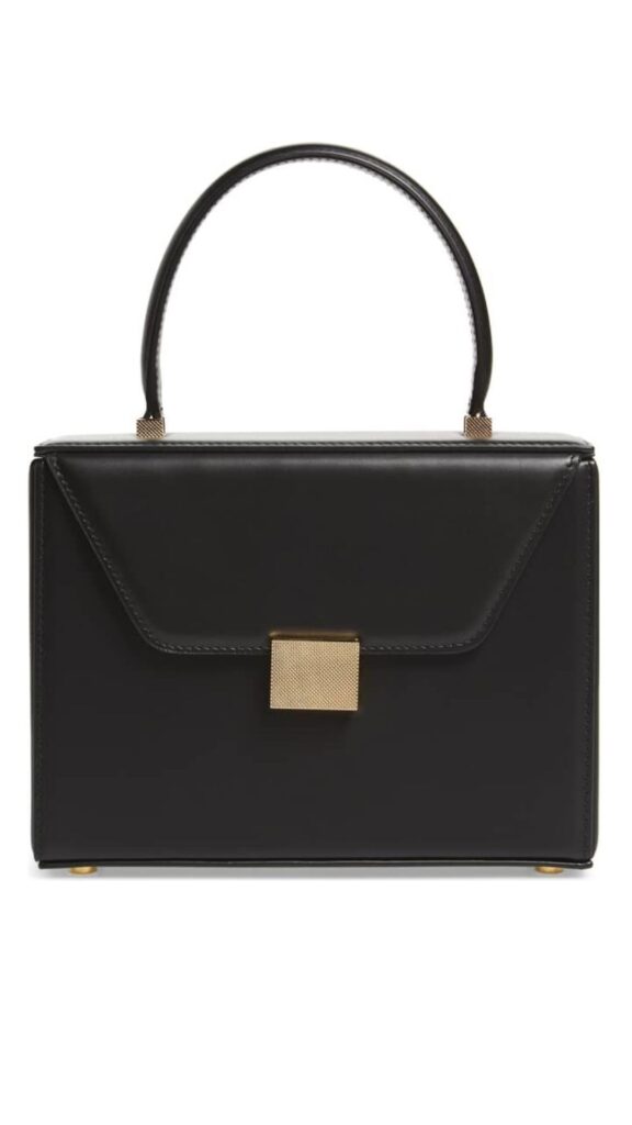 The Victoria Beckham Black Mini Vanity Bag features a structured rectangular silhouette with a top handle and a minimalist aesthetic. It is crafted from sleek black leather, accented by a gold mesh clasp and subtle gold feet on the base. The bag's clean lines and sophisticated design make it an elegant accessory for any occasion.