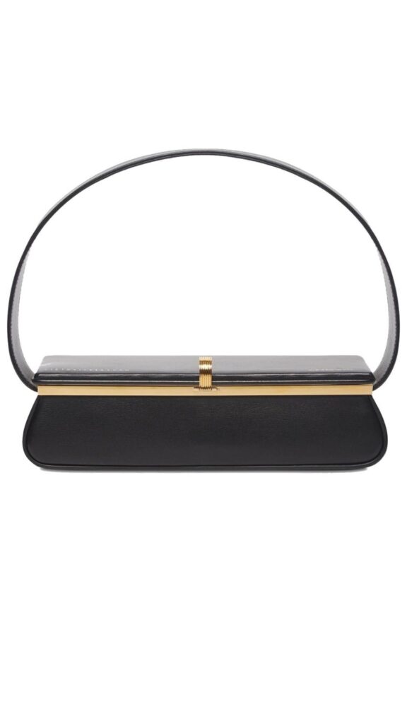 The Victoria Beckham Powder Box Leather Tote features a sleek, rectangular silhouette with a minimalist design. It is crafted from smooth black leather, accented by a subtle gold clasp at the top and a structured handle. The overall look exudes sophistication, making it a versatile accessory for various occasions.